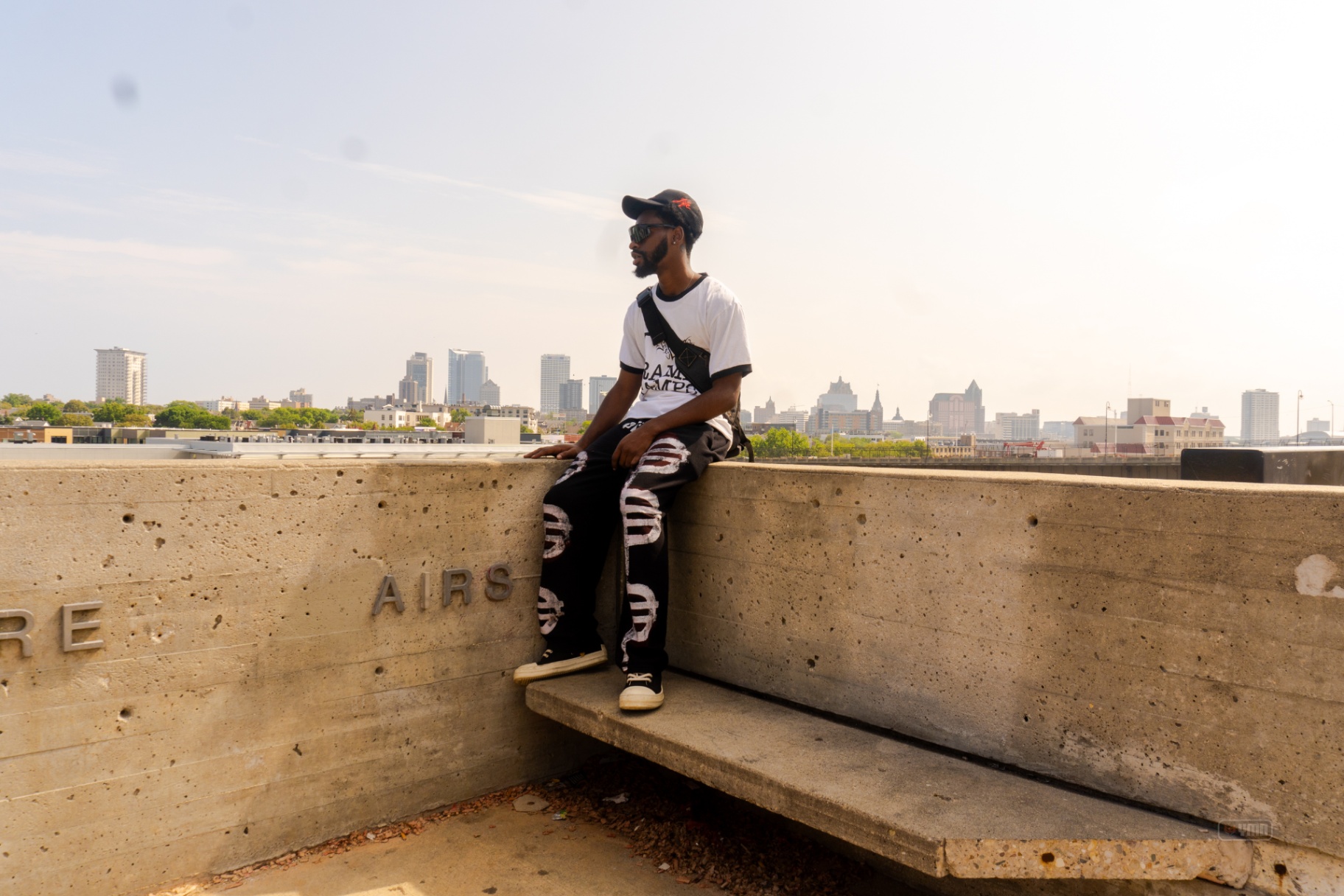 Man seated on a concrete ledge with the Milwaukee skyline behind