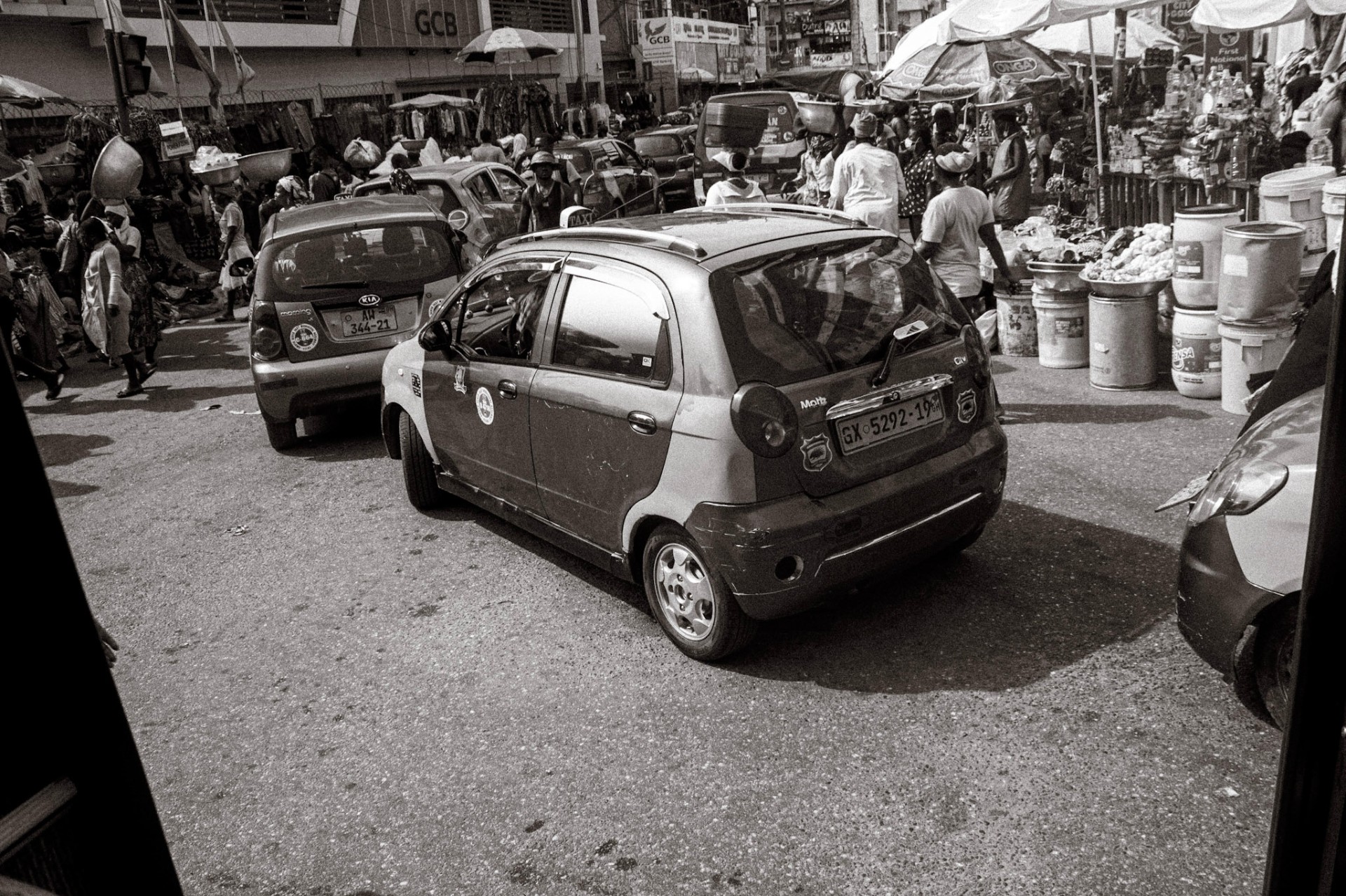 Taxis threading through a busy Accra market street