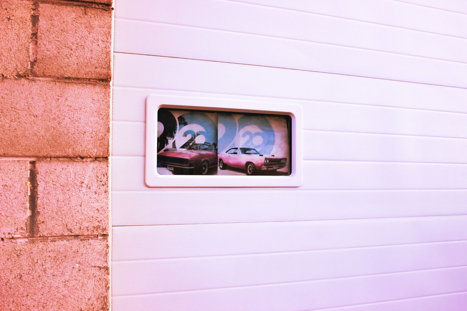 Muscle car print framed behind a garage window on a brick wall