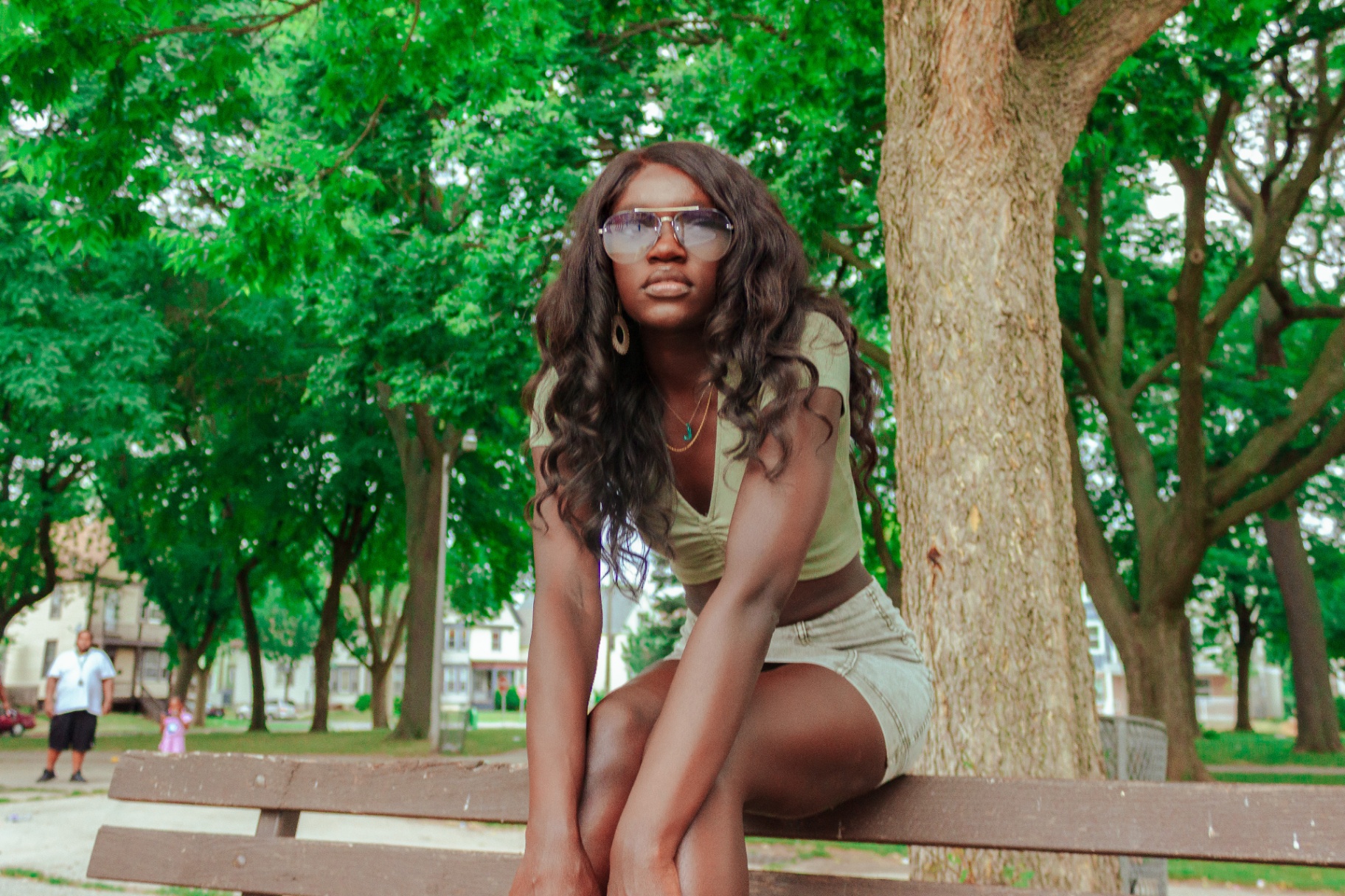 Woman leaning forward on a park bench beneath green summer trees