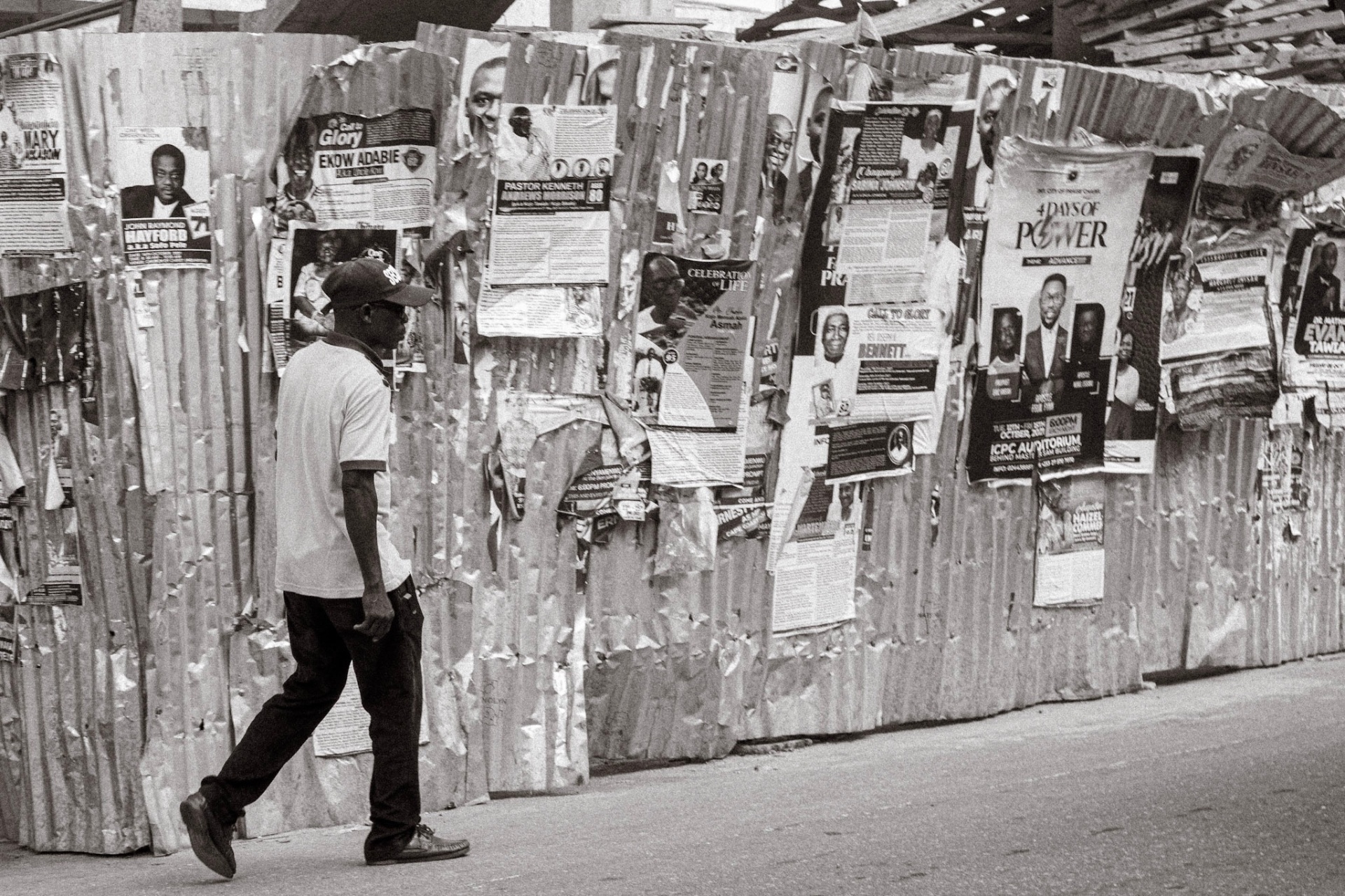 Man walking past a corrugated fence covered in funeral and event posters