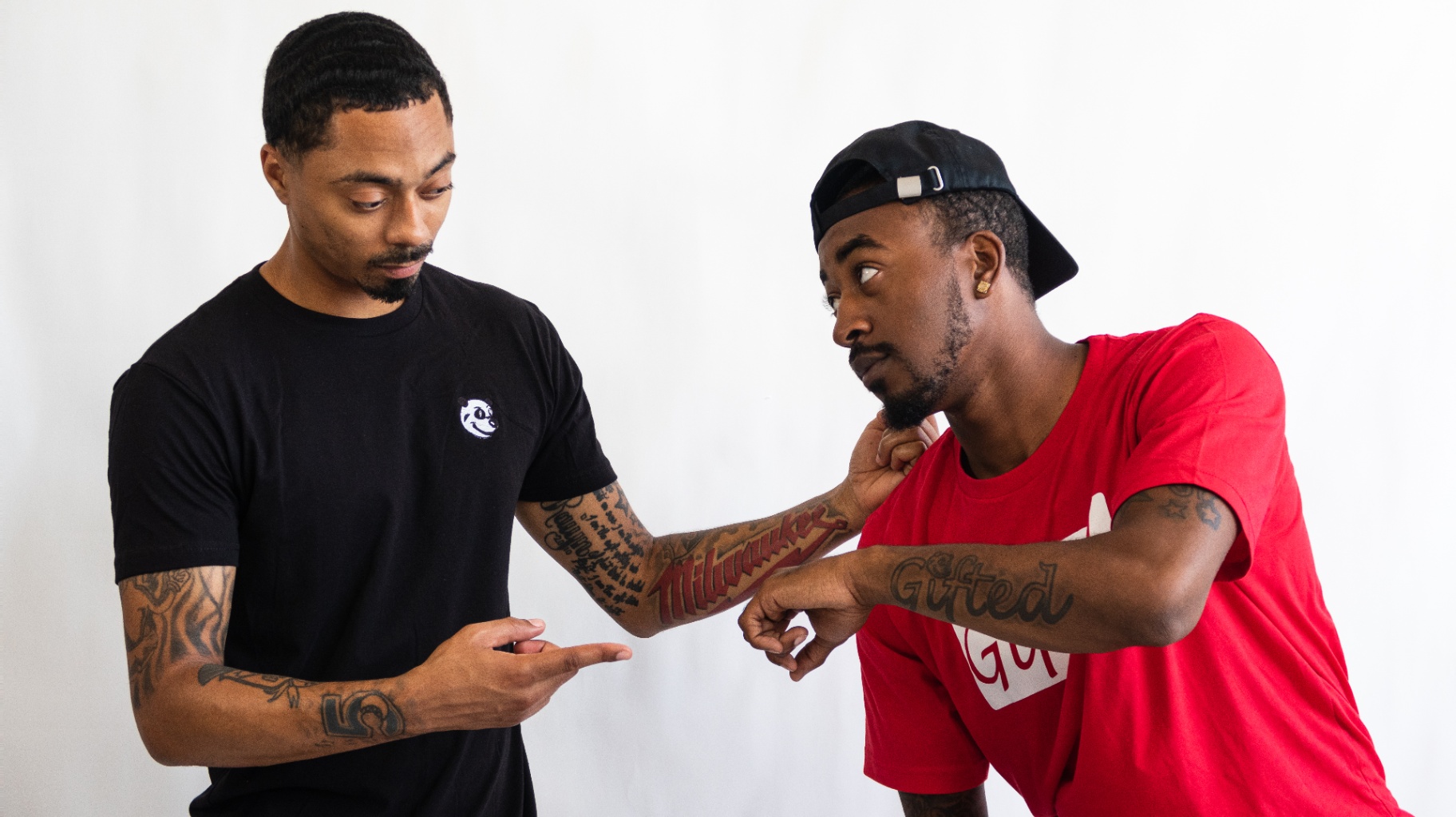 Two men comparing Milwaukee and Gifted forearm tattoos on a white backdrop
