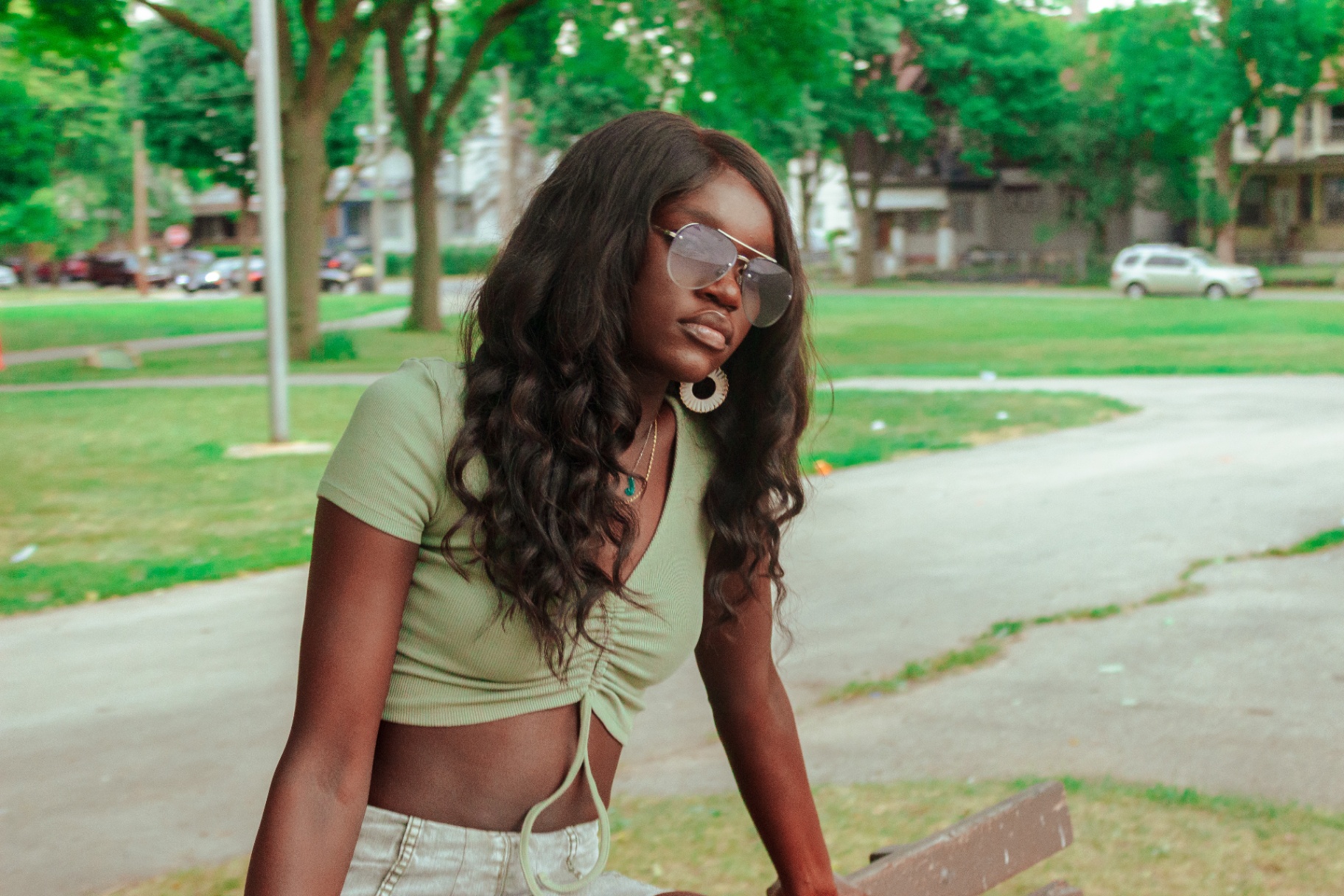 Portrait of a woman in aviators and a sage crop top on a Milwaukee park bench