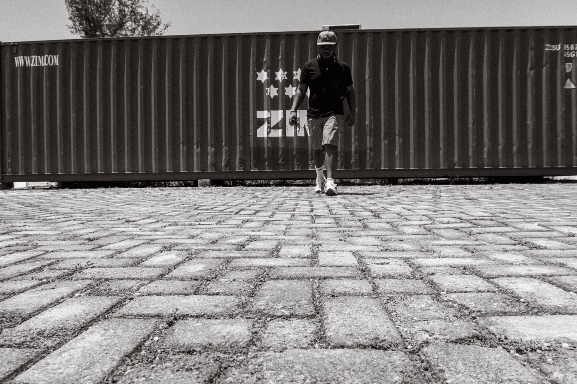 Photographer walking across cobblestones past a ZIM container