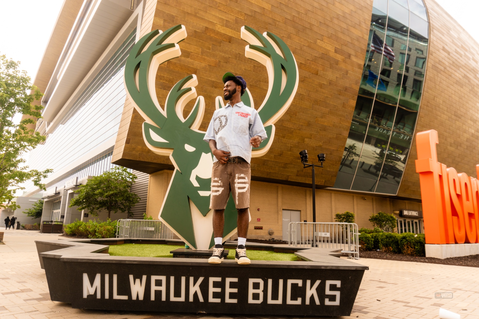 Man posing on the Bucks statue plinth outside Fiserv Forum