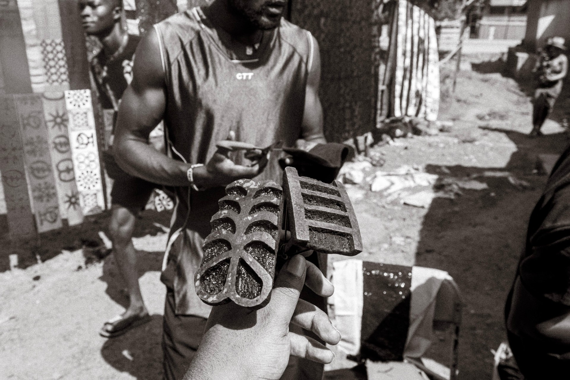 Vendor holding two cast-iron coal pots in an Accra market