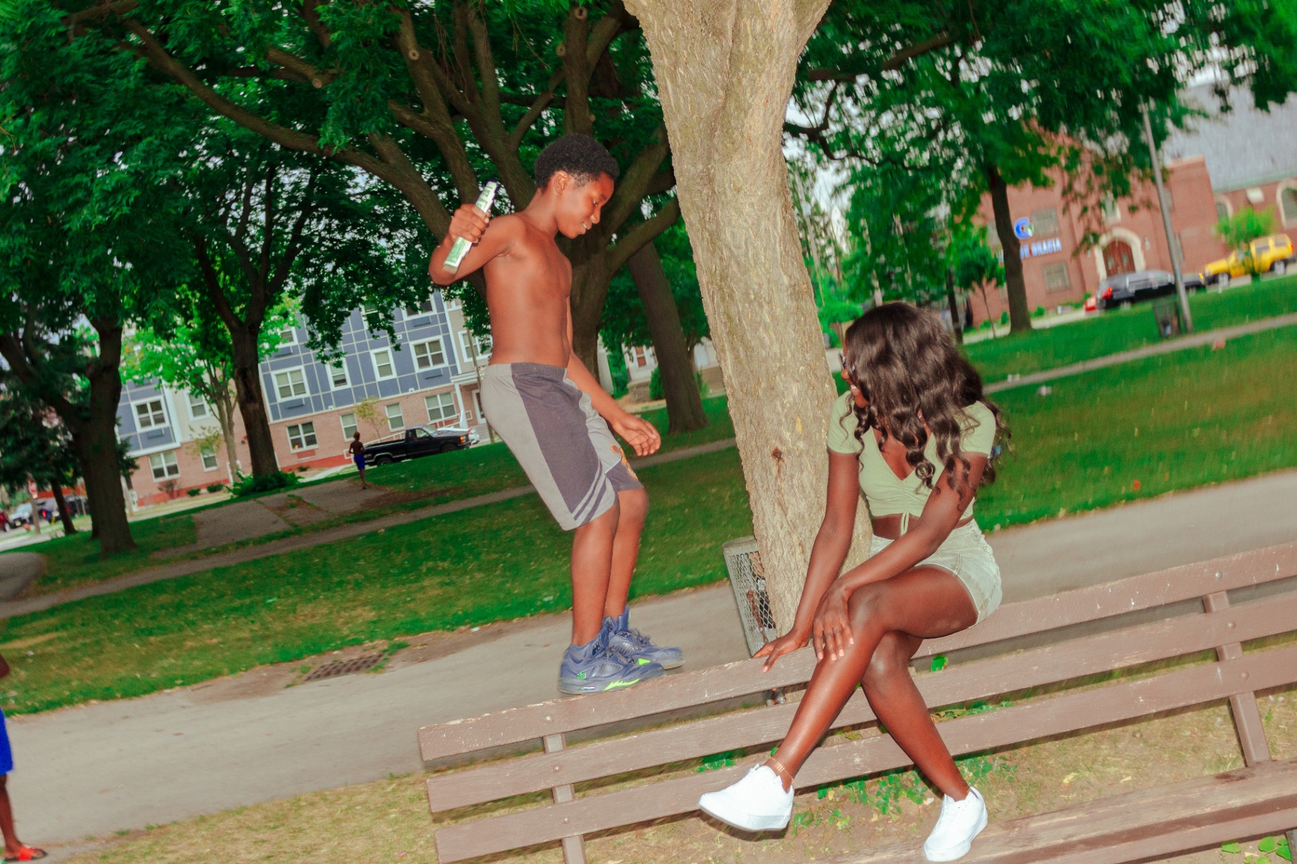 Child in Jordans stepping onto a park bench beside a seated woman