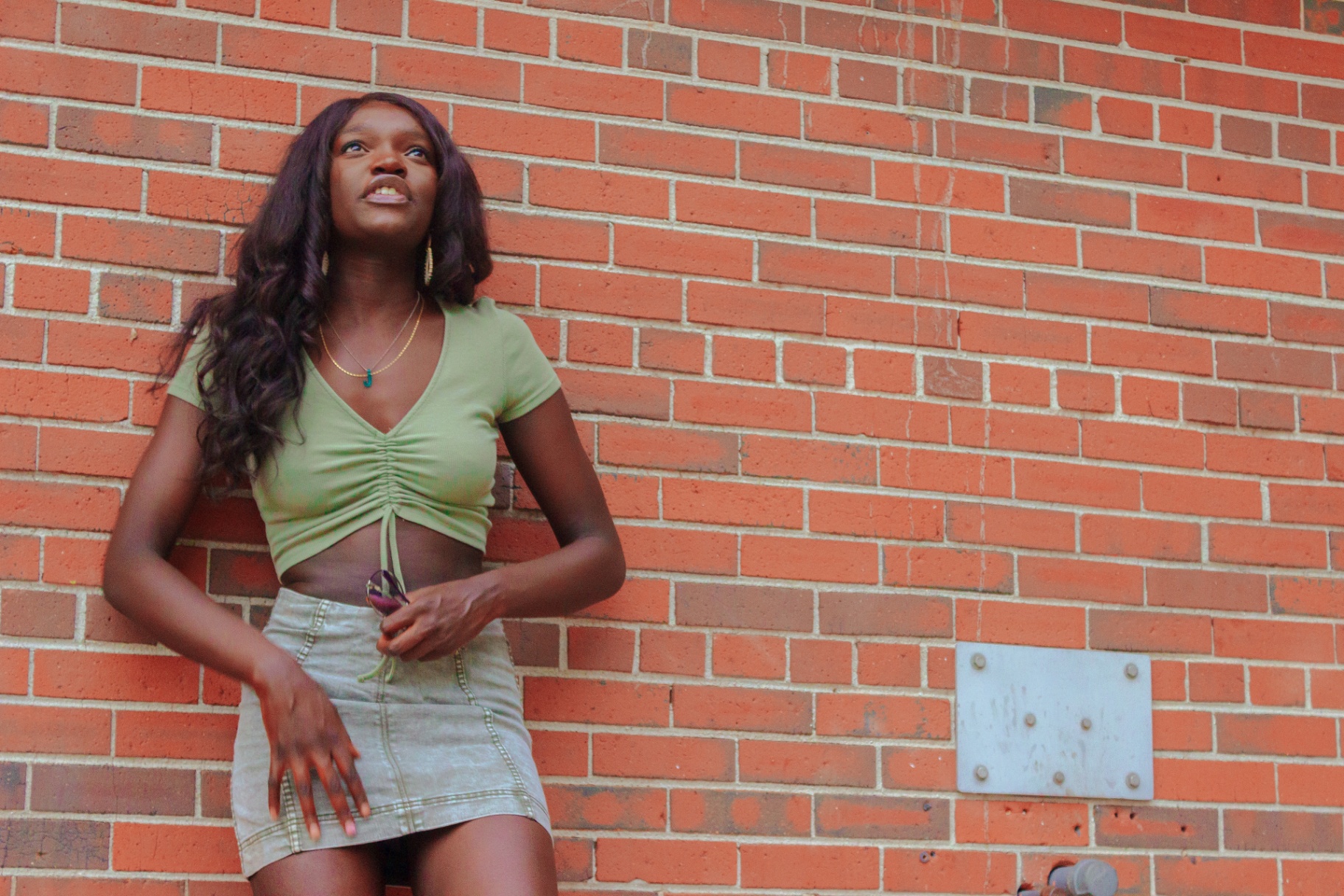 Woman in sage crop top leaning against a red brick wall
